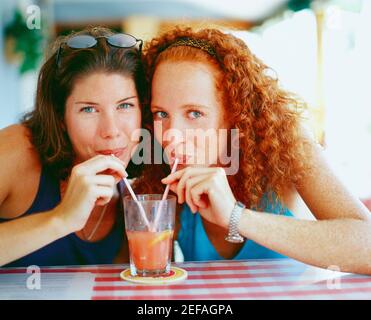 Portrait de deux jeunes femmes buvant du jus d'un verre avec pailles, Bermudes Banque D'Images