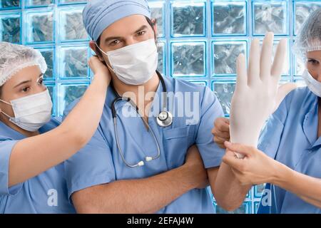 Deux femmes chirurgiens ajustant le gant chirurgical et le masque chirurgical de un médecin de sexe masculin Banque D'Images