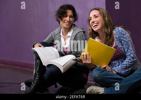 Deux jeunes femmes tenant leurs manuels scolaires et assis dans un couloir Banque D'Images