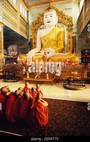 Vue arrière des moines priant devant une statue de Bouddha, Sagaing, Myanmar Banque D'Images