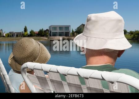 Vue arrière d'un couple assis sur des chaises au au bord du lac Banque D'Images