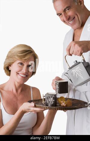 Portrait d'un homme âgé qui verse du thé bouilloire dans la tasse avec une femme mûre tenant un plateau Banque D'Images