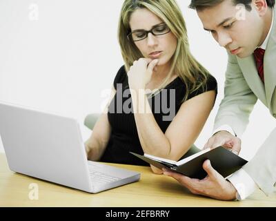 Gros plan d'un homme d'affaires et d'une femme d'affaires devant un ordinateur portable et regardant un journal Banque D'Images