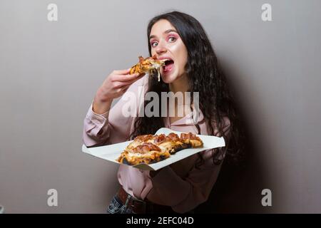 Fille de coursier manger la pizza pinsa romana cuisine italienne gastronomique sur fond gris. Contenant un plat traditionnel de scocchiarella. Livraison de nourriture de pizzeri Banque D'Images