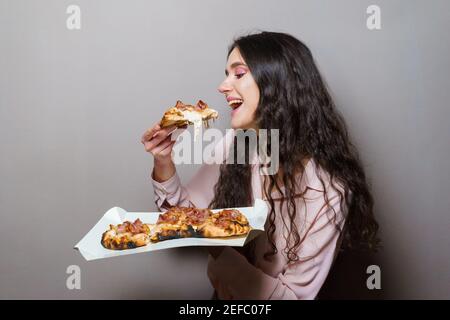 Fille de coursier manger la pizza pinsa romana cuisine italienne gastronomique sur fond gris. Contenant un plat traditionnel de scocchiarella. Livraison de nourriture de pizzeri Banque D'Images