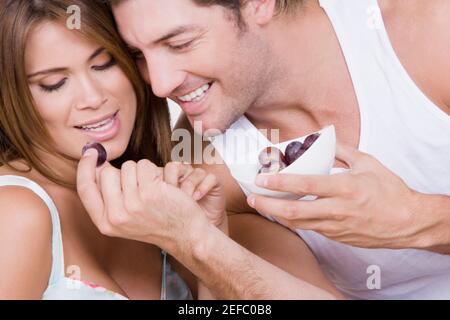 Homme adulte moyen nourrissant des raisins à une jeune femme et sourire Banque D'Images