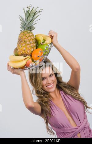 Portrait d'une jeune femme tenant un panier assorti fruits et sourire Banque D'Images