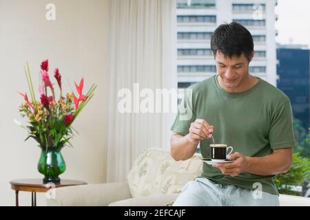 Homme adulte moyen remuant le thé avec une cuillère à café Banque D'Images