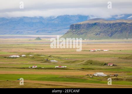 Vue sur la campagne islandaise avec ses fermes au pied des montagnes. Banque D'Images