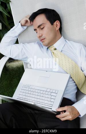 Homme d'affaires dormant sur une chaise longue avec un ordinateur portable ses genoux Banque D'Images