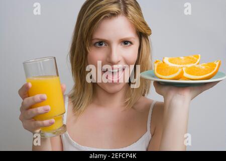 Portrait d'une adolescente portant une assiette d'oranges et un verre de jus d'orange Banque D'Images