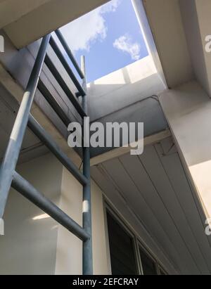 Échelle métallique près de l'extérieur de la salle de réunion pour grimper sur le toit du bâtiment de bureau, vue sur le ciel depuis la marche basse avant l'ascension. Banque D'Images