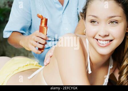 Vue en coupe centrale d'un homme appliquant une lotion de bronzage Un jeune femme est de retour au bord de la piscine Banque D'Images