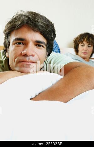Portrait d'un homme mûr allongé sur le lit avec une femme mature en arrière-plan Banque D'Images