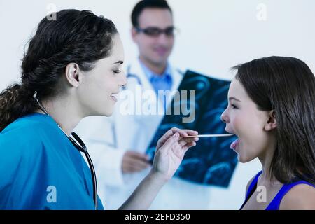 Profil d'une femme médecin examinant une petite bouche avec un dépresseur de langue Banque D'Images