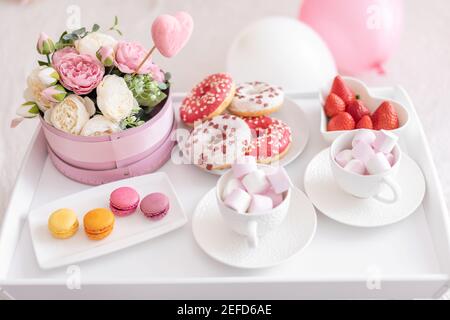 Fleurs et bonbons sur la table blanche et ballons sur le lit. Cadeau pour la Saint-Valentin ou le 8 mars ou pour la fête des mères ou l'anniversaire Banque D'Images