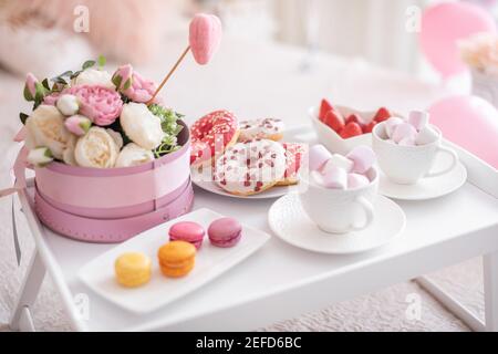 Fleurs et bonbons sur la table blanche et ballons sur le lit. Cadeau pour la Saint-Valentin ou le 8 mars ou pour la fête des mères ou l'anniversaire Banque D'Images