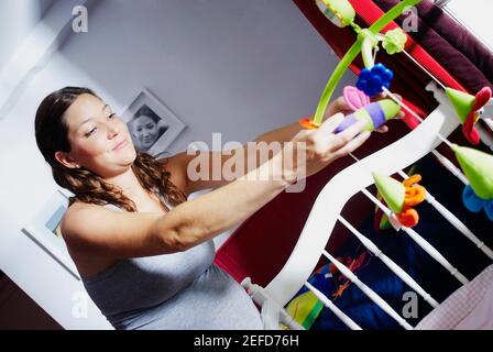 Gros plan d'une jeune femme enceinte ajustant des jouets dans un lit enfant Banque D'Images