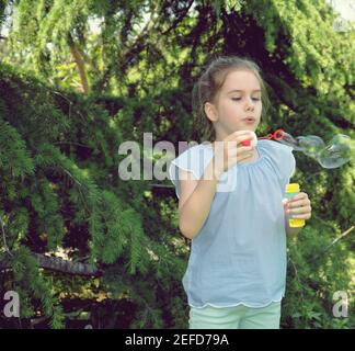 Fille blonde souriante et bulles soufflantes dans le parc avec des arbres verts en arrière-plan. Mise au point sélective Banque D'Images