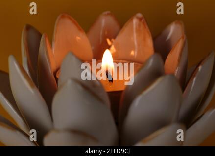 prise de vue macro avec grande profondeur de champ de bougie mèche avec flamme dans un porte-bougie fleur de lotus un fond jaune profond Banque D'Images