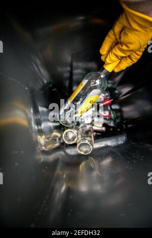Personne avec un gant jaune plaçant des contenants en verre dans un nouveau bac de recyclage de la roue en verre. Banque D'Images