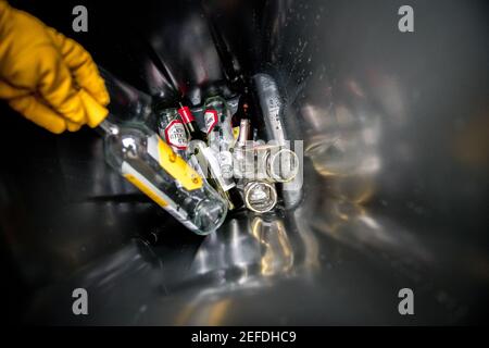 Personne avec un gant jaune plaçant des contenants en verre dans un nouveau bac de recyclage de la roue en verre. Banque D'Images
