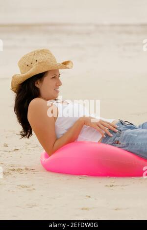 Profil de la jeune femme allongé sur un anneau gonflable à la plage Banque D'Images