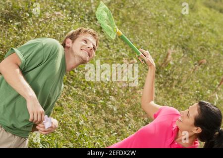 Vue en grand angle d'une jeune femme tenant un papillon Filet sur une tête de jeune homme Banque D'Images
