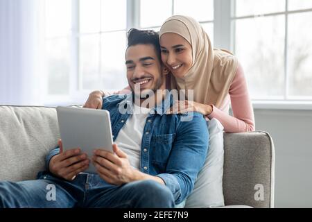 Beau couple musulman barbu gars et jeune femme dans hijab ayant la vidéoconférence via la tablette numérique tout en restant à la maison pendant la pandémie Covid-19, m Banque D'Images