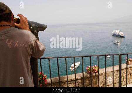 Vue arrière d'un homme regardant à travers un binoculaire à pièces, baie de Naples, via Aniello Califano, Sorrento, péninsule de Sorrentine, Province de Naples, Campanie, Italie Banque D'Images