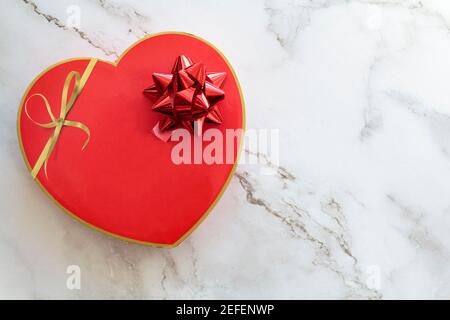 Vue de dessus de la boîte cadeau en forme de coeur rouge avec un noeud sur fond de marbre blanc avec espace de copie Banque D'Images