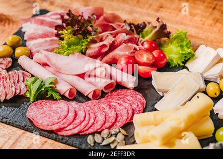 Coupes froides de différents types de saucisses sur un noir Plat sur une table en bois avec des légumes.différents types de saucisses au fromage servies sur le woo Banque D'Images