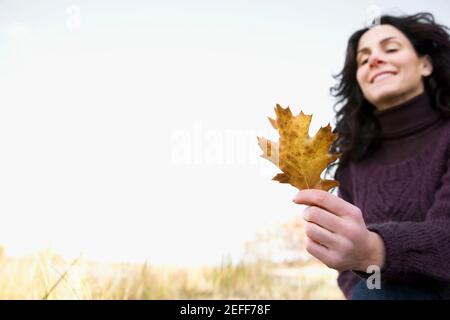 Gros plan d'une femme mature tenant une feuille d'érable et sourire Banque D'Images