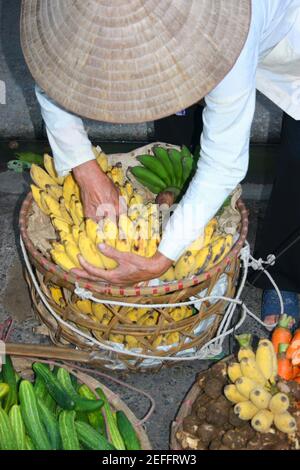 Vue en grand angle d'un homme organisant des bananes dans un panier, Hanoi, Vietnam Banque D'Images