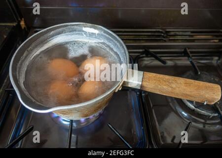 Les œufs cuisent dans une casserole d'eau bouillante sur une table de cuisson à gaz. Banque D'Images