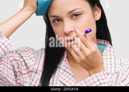 Portrait of a young woman measuring sa température avec un thermomètre et tenant une poche de glace sur la tête. Banque D'Images