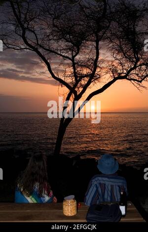 Homme et femme regardant le coucher du soleil sur la mer, Pakini Nui Wind Project, South point, Big Island, Hawaii Islands, Etats-Unis Banque D'Images