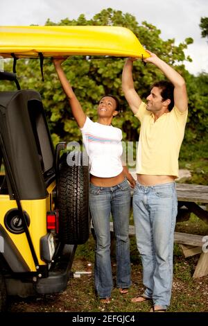 Une jeune femme et un homme de taille moyenne adulte chargeant un kayak sur une jeep Banque D'Images