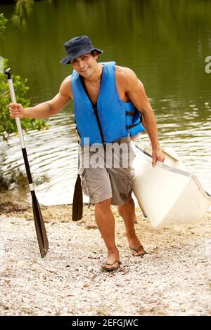 Vue en grand angle d'un homme adulte de taille moyenne portant un kayak et un oar Banque D'Images