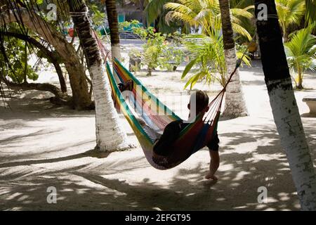 Vue arrière d'un homme allongé dans un hamac, Coral Cay, Dixon Cove, Roatan, Bay Islands, Honduras Banque D'Images