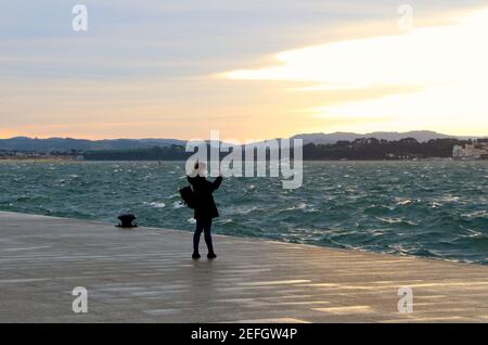 Femme debout prenant une photo sur son téléphone portable d'une mer agitée dans la baie de Santander à l'aube hiver Santander Cantabria Espagne Banque D'Images