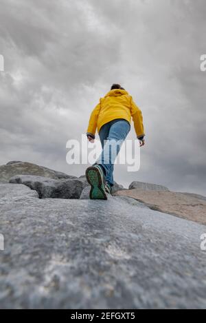 Vue arrière d'une femme qui monte sur une colline de rocher contre un ciel nuageux et spectaculaire. Prise de vue verticale avec un grand espace de copie en bas. Banque D'Images