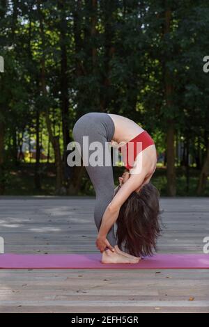 30s belle femme portant un débardeur rouge et des leggings gris sport en plein air dans le parc le jour de l'été, faisant debout de la tête aux genoux posture, UT Banque D'Images