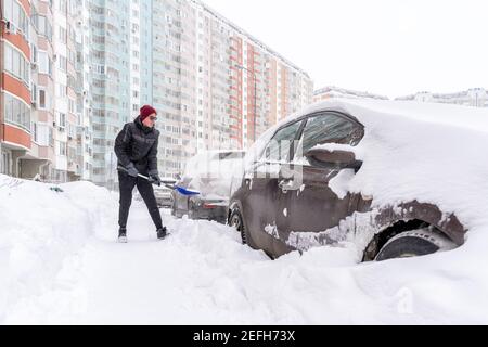 un homme creuse sa voiture d'une captivité de neige. les voitures sont garées près d'un bâtiment de plusieurs étages Banque D'Images