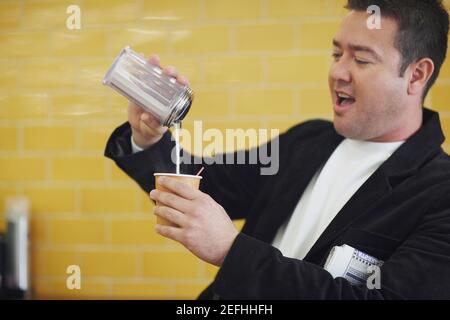Homme adulte moyen versant du lait dans une tasse jetable Banque D'Images