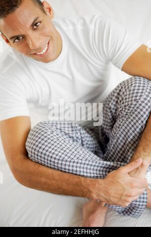 Portrait d'un homme adulte moyen assis sur le lit et souriant Banque D'Images