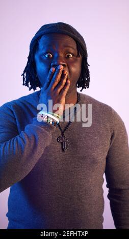 Surpris l'homme africain avec des dreadlocks mettant la main sur sa bouche. Secret découvert. . Photo de haute qualité Banque D'Images