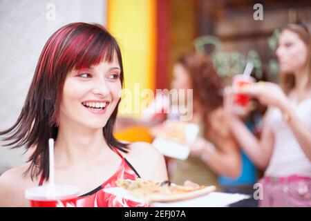 Jeune femme tenant une assiette avec une boisson froide et une tranche de pizza Banque D'Images