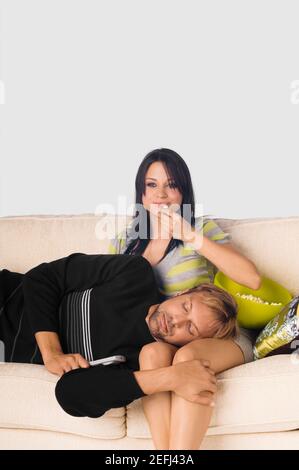 Mid adult man sleeping sur les genoux d'une jeune femme mangeant popcorns Banque D'Images