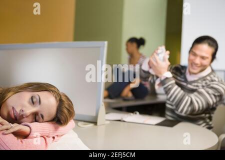 Une jeune femme se met à la sieste sur un bureau avec un jeune homme sourire en arrière-plan Banque D'Images